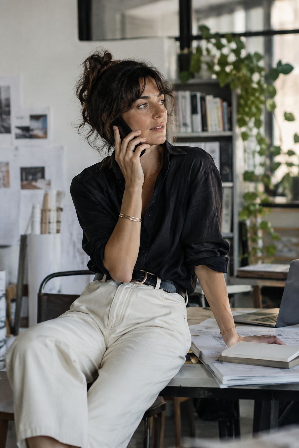 Une dirigeante assise sur le bord de son bureau, au téléphone, dans son atelier.